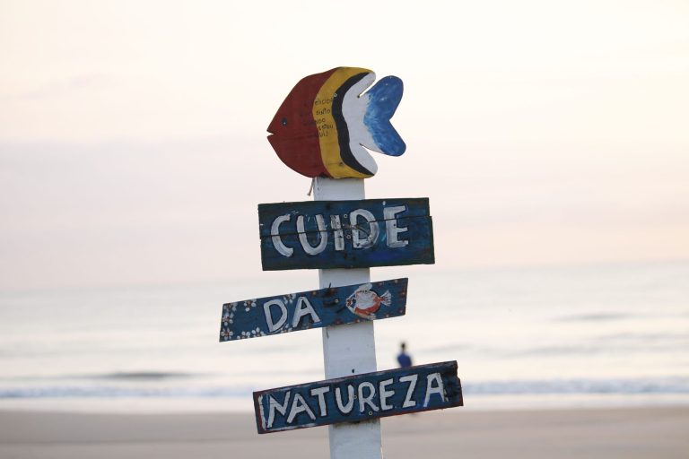 Certificação Bandeira Azul chega a 75 praias e marinas brasileiras em 2026/2027 Placa colorida em Guaratuba, no Paraná, incentiva o cuidado com a natureza diante do oceano ao nascer do sol.